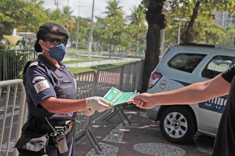 Guarda Municipal usando máscara e luga entrega folheto na mão de uma pessoa. #Paratodosverem