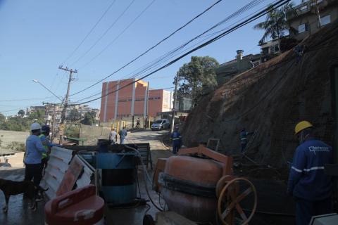 Máquinas estão na pista ao lado de encosta. Homens estão em torno. #Paratodosverem