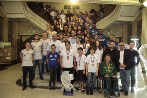 Atletas, técnicos e autoridades posam para foto na escadaria do hall da Prefeitura. #Pracegover