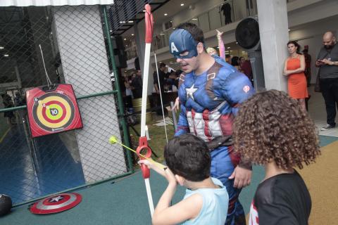 menino com arco e flecha observado por homem vestido de super herói #pracegover