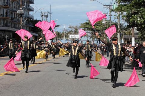 Banda desfila e seus integrantes fazem coreografia com bandeiras. #Pracegover