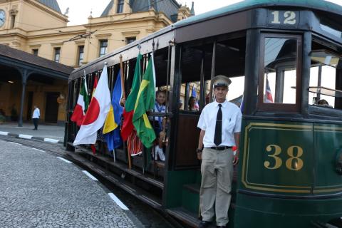 Bonde circula com bandeiras de nações para fora na lateral. #pracegover