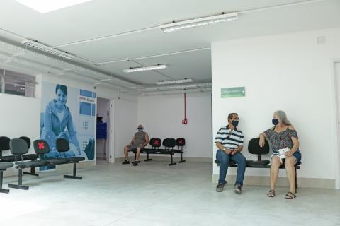 Sala de espera para atendimento. Há três pessoas sentadas. #Paratodosverem