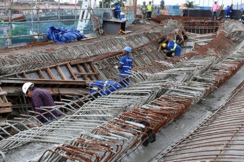 Estrutura de ferragens e concreto com homens trabalhando. #Pracegover