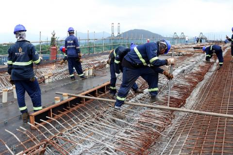 Homens trabalham em concretagem. Eles estão sobre estrutura de ferragens. #Pracegover