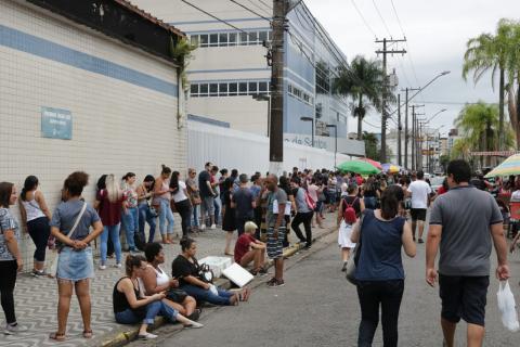 Inscritos aguardam abertura dos portões sentados na calçada e em pé. #pracegover