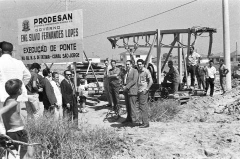 Homens em volta da placa de construção da ponte do Rio São Jorge. #pracegover