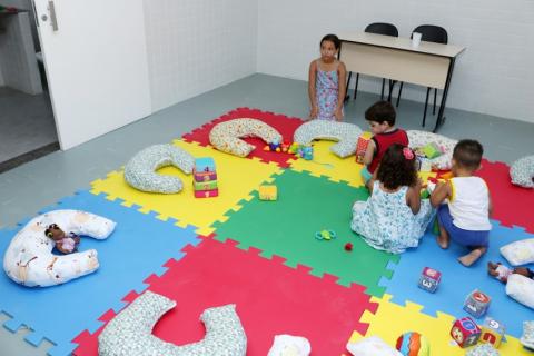 Crianças brincam sentadas em tapete colorido de EVA. #pracegover