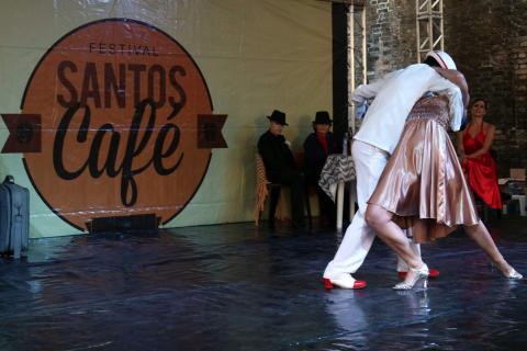 Balé da Cidade se apresenta no palco. Casal está dançando. O rapaz enlaça a moça e curva seu tronco para baixo. #Pracegover
