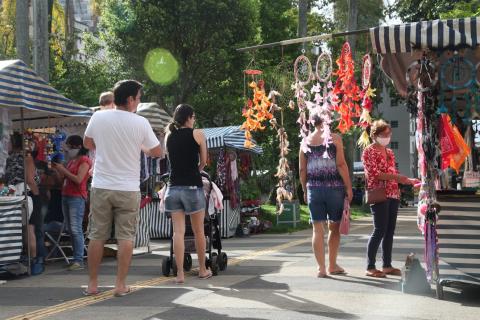 Visitantes circulam pela praça onde há barracas de artesanato. #Paratodosverem