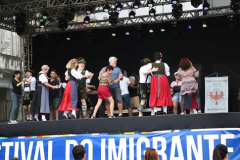 Dançarinos alemães chamam público para participar no palco. #pracegover