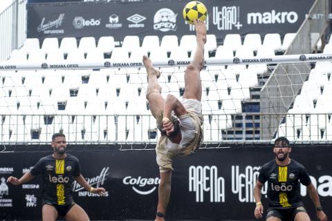 jogador salta para chutar a bola e adversários observam #paratodosverem