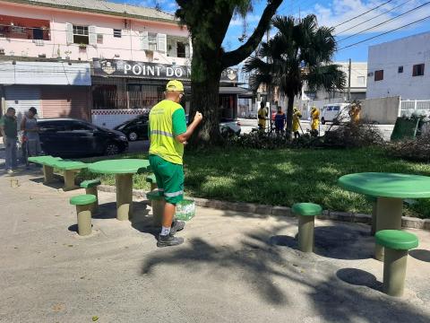 Homem pinta mesa de jogos em praça. Há outras mesas recém´-pintadas. #paratodosverem