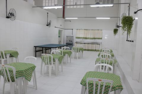 Sala branca com várias mesas com toalhas verdes e cadeira. #paratodosverem