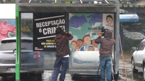 homem está de costas para a imagem. Ele cola adesivos em ponto de ônibus. #paratodosverem