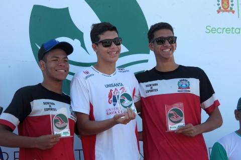 Gabriel Santos Galuzzi (centro); Daniel Rezende Fidelis (à esquerda) e Ítalo Bressane da Costa (à direita), todos no pódio segurando troféus. #paratodosverem