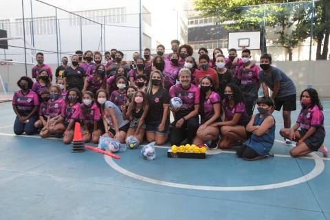 grupo de participantes do projeto e o ator, todos uniformizados, posa para foto no meio da quadra. #paratodosverem