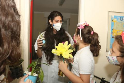 alunos entregam flores para uma mulher que está usando avental branco. #paratodosverem