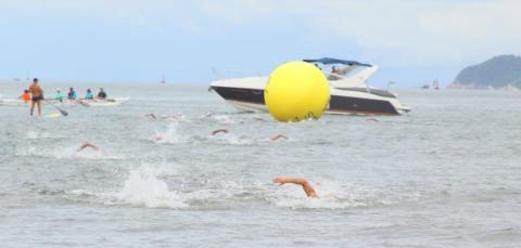 Atletas nadam no mar santista com embarcação de apoio ao fundo. #pracegover