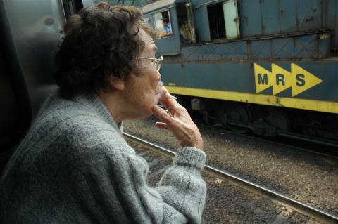 Senhora com traços orientais fuma e observa trem #paratodosverem