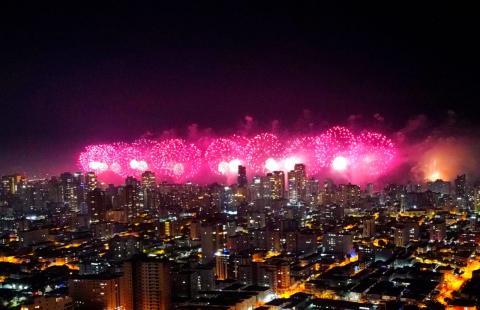 Queima de fogos, na cor rosa, com prédios em primeiro plano.