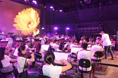 Orquestra Sinfônica com telão ao fundo.