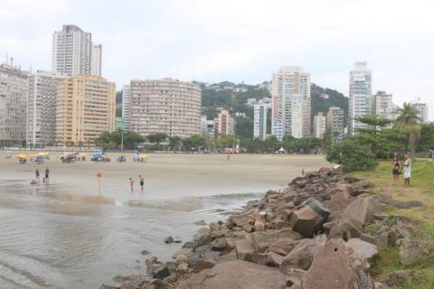 molhe de pedras do emissãrio com vista para trecho de areia e pedras ao fundo. #paratodosverem