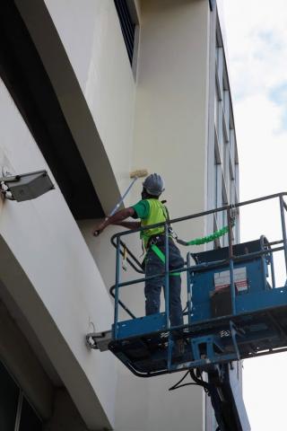 Homem em andaime elevado pinta fachada de prédio. #paratodosverem 