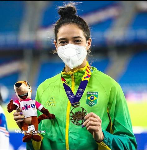 atleta segura medalha e mascote de pelucia dos jogos #paratodosverem