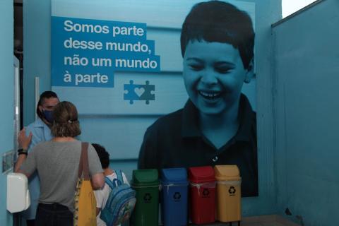 Sala de entrada da unidade com foto de criança e a frase na parede: Somos parte desse mundo. Não um mundo à parte. #paratodosverem