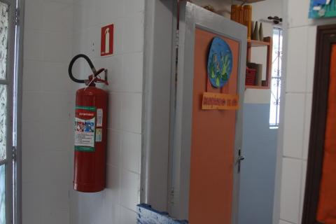 extintor de incêndio afixado em parede ao lado de porta de sala de aula. #paratodosverem