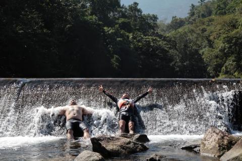 dois homens recostados em cachoeira se banhando. #paratodosverem