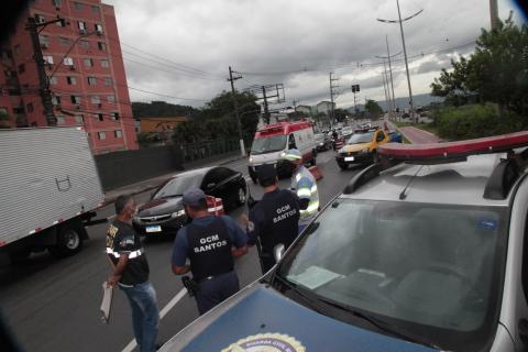 Equipe de fiscalização faz barreira na entrada da cidade. Em primeiríssimo plano há uma viatura da guarda. Ao fundo, os carros na pista. #Paratodosverem