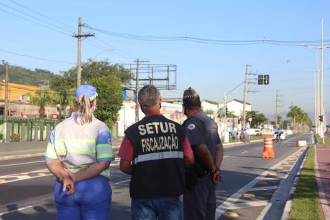 Agentes da CET, Do turismo e um policial militar estão de costas para foto e observam via. #paratodosverem