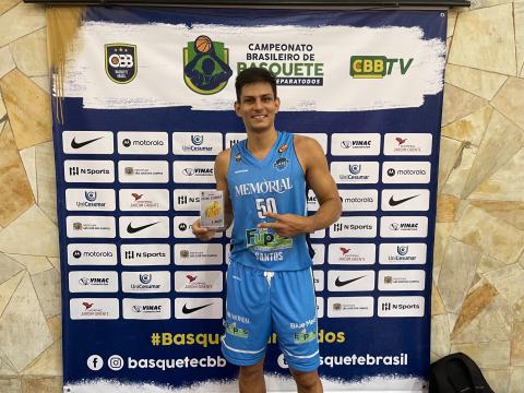 O ala Jonathan posa para foto segurando troféu. Atrás dele há um painel de patrocinadores. #paratodosverem