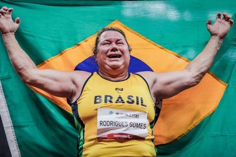 A atleta à frente da bandeira do brasil abre os braços emocionada. #paratodosvere