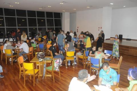 Salão com mesas e cadeiras e várias pessoas sentadas. #paratodosverem