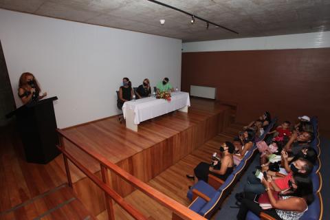 Jovem faz discurso em pé no púlpito observadas pelo público na plateia. #pratodosverem