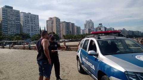 guarda conversa com homem na faixa de areia. Há uma viatura ao lado. #paratodosverem