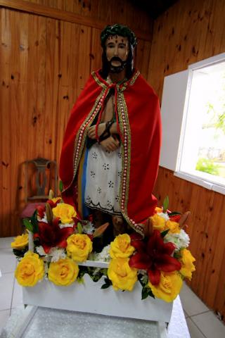 Imagem de Bom Jesus dentro da capela rodeada de flores. #pratodosverem