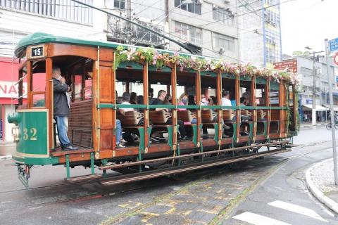 Pessoas dentro de bonde que circula pela rua #paratodosverem