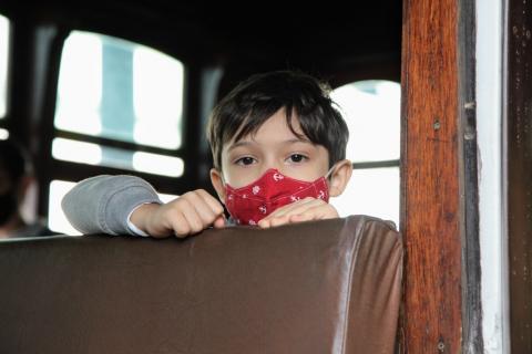 detalhe de menino com máscara sentada em um banco do bonde. #paratodosverem
