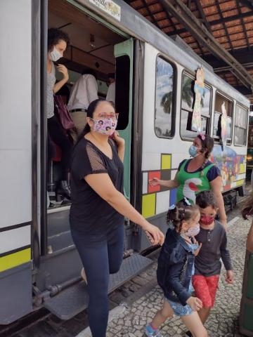 mulher sai de bonde segurando a mão de uma criança. Outras crianças também saem do veículo. #paratodosverem