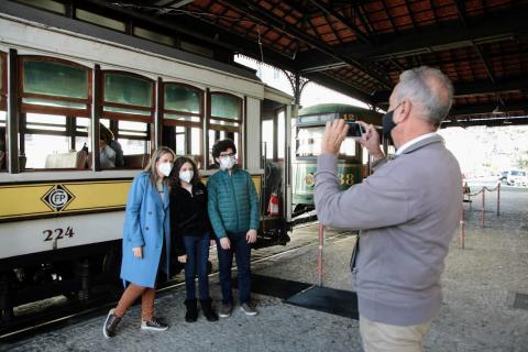 três pessoas à frente do carro de bonde na estação são fotografadas no celular de um homem. #paratodosverem