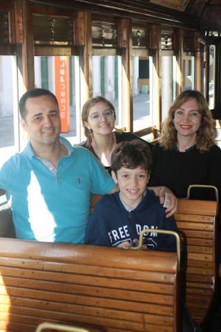 quatro pessoas de uma família estão sentadas nos bancos do bonde. #paratodosverem