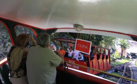 Bonde funicular com duas pessoas no carro que desce. O bonde que sobe está vindo. Ambos estão próximos de se cruzar. #paratodosverem