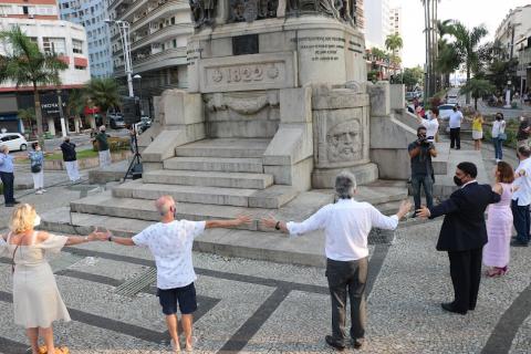 pessoas dão as mãos em torno de monumento. #paratodosverem