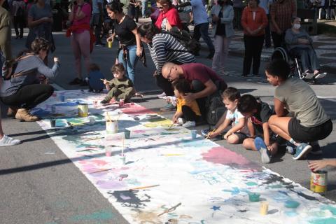 crianças e adultos pintam sobre grande lona estendida no chão da avenida. #paratodosverem
