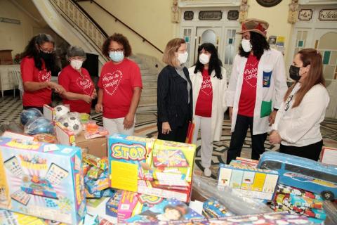 movimentação de voluntárias diante de mesas cheias de brinquedos. Um homem com chapéu faz parte do grupo. #paratodosverem