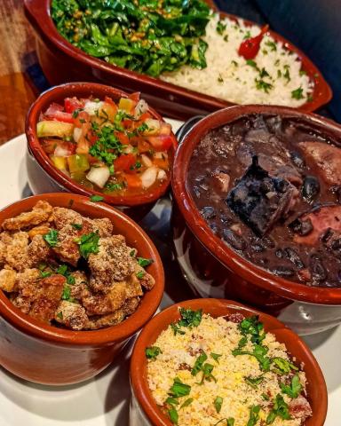 Porções de feijoada: farofa, torresmo, vinagrete, feijão preto e arroz. #pracegover